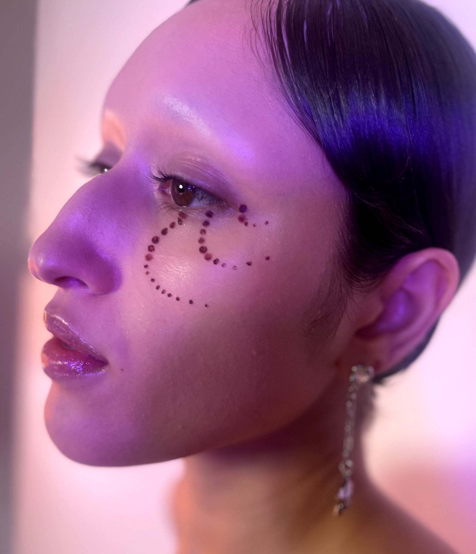 Side view of Model with medium skin tone with Deepdive colorpot in aeonium in a dot pattern from their lower left eye down their cheek