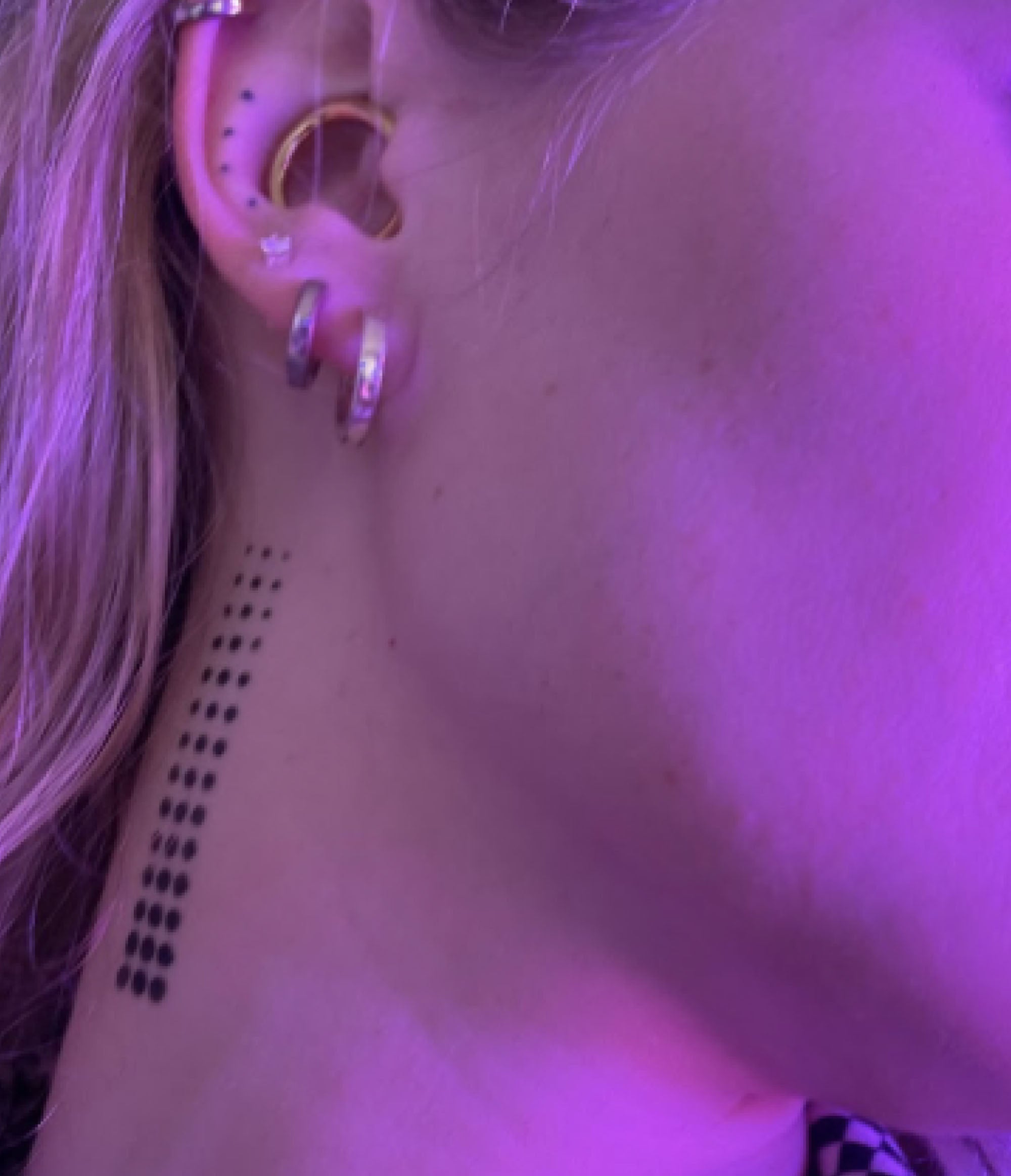 A close up of skinweare on a girls neck and bottom of ear in pink lighting. On her neck there is a black dot pattern in a 3 by 15 grid made by the corvid deepdive product..