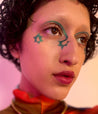 Model with medium skin tone wearing a Colorwand in figeater under brows and inner nose with a star pattern at the end. Star on upper cheek bone.