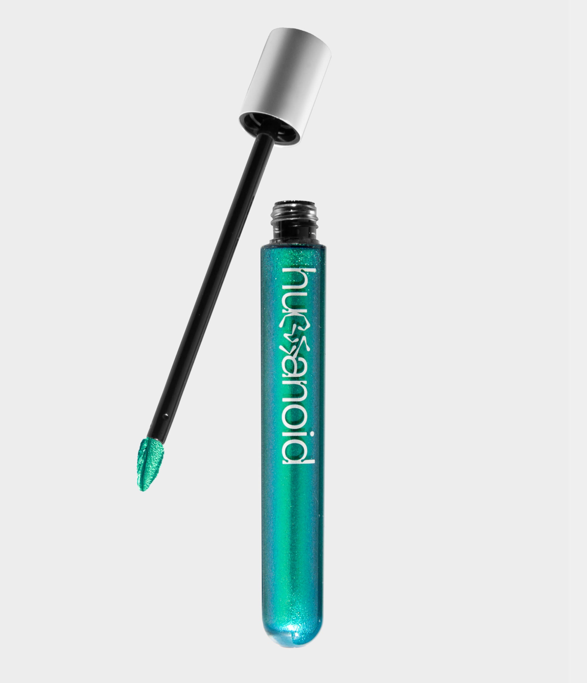 A transparent tube of shimmery green liquid makeup with an unscrewed silver cap sitting next to it. A doe foot makeup applicator coated in green makeup extends out of the cap.