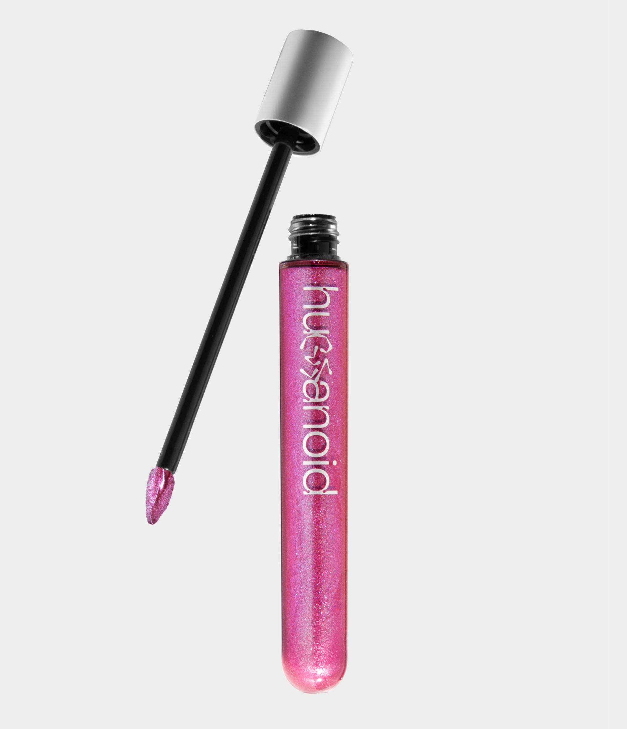 A transparent tube of shimmery pink liquid makeup with an unscrewed silver cap sitting next to it. A doe foot makeup applicator coated in pink makeup extends out of the cap.