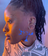 Side view of a model with a dark skin tone wearing Deepdive in Benitoite along their left cheek and neck in a geometric pattern with triangles.