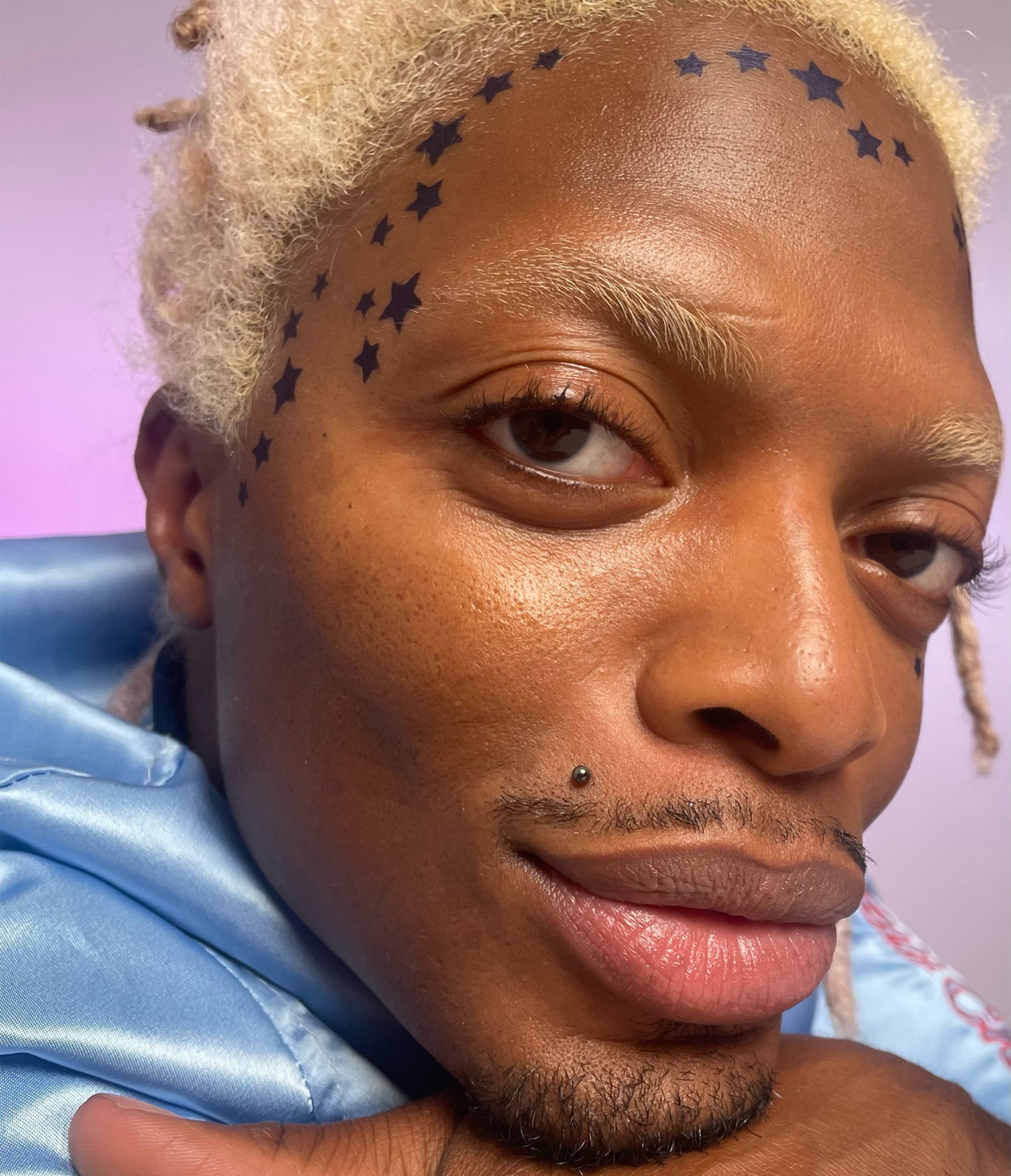 Model with dark skin tone wearing Wooly Bluecurls in a star pattern across the top of their forehead and temple