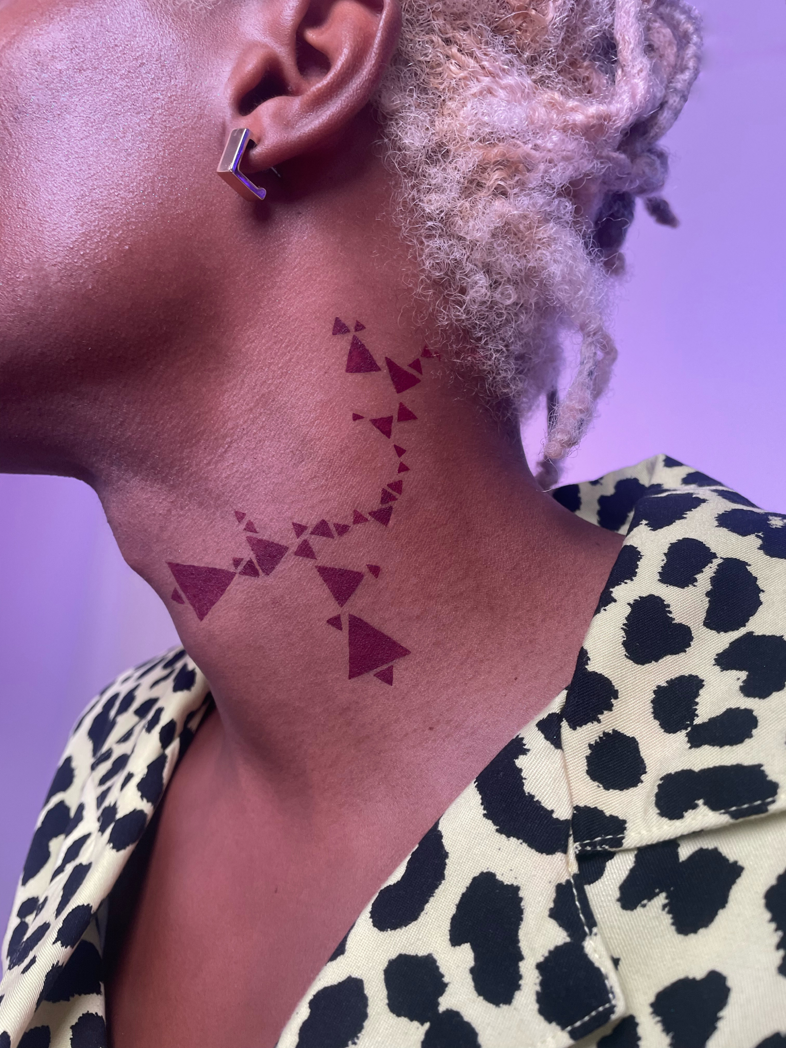 Side view of a model with a dark skin tone wearing deep dive in Aeonium along the side of their neck in a geometric pattern with triangles.